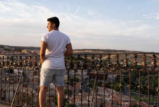 Boy with white T-shirt and brown hair on his back facing a village