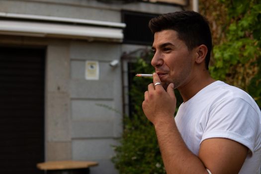 Man smoking in the street with a white T-shirt and brown hair