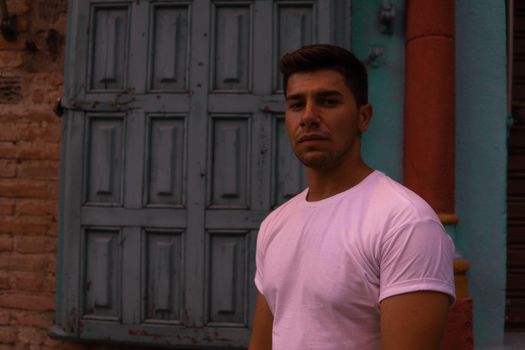 Man with a white T-shirt and a brown door in the background modeling and intense look