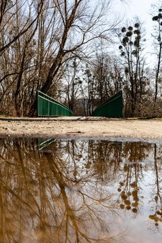 Long concrete bridge over river with green metal railing reflected in small puddle