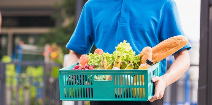 Asian grocery store delivery man wearing blue uniform and face mask protect he delivering fresh food vegetable in plastic box at door front home after coronavirus outbreak, back to new normal concept