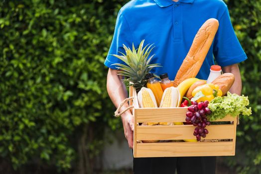 Asian man farmer wears delivery uniform he holding full fresh vegetables and fruits in crate wood box in hands ready give to customer harvest organic food on the garden place green leaves background