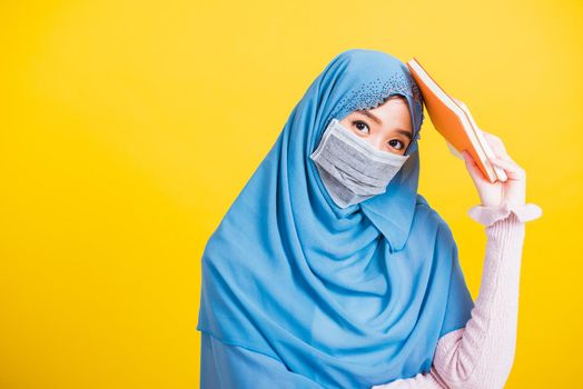 Asian Muslim Arab, Portrait of young woman religious wear veil hijab and face mask protective to prevent coronavirus she student hold books on hand, isolated on yellow background, Back to college