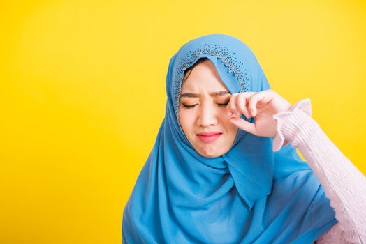 Asian Muslim Arab, Portrait of happy beautiful young woman religious wear veil hijab she sad crying using hand wiping tears in her eyes, studio shot isolated on yellow background with copy space