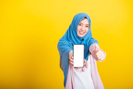 Asian Muslim Arab woman Islam wear veil hijab funny smile she showing blank screen smart mobile phone and point screen, studio shot isolated on yellow background
