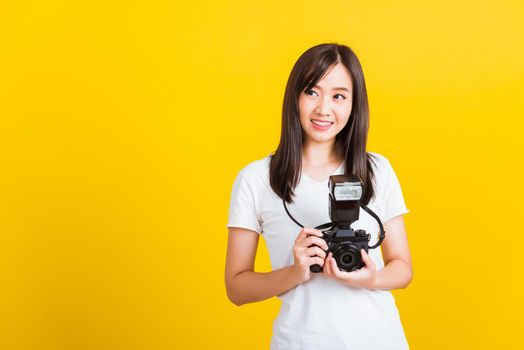 Portrait of happy Asian beautiful young woman photographer holding vintage digital mirrorless photo camera on hands, studio shot isolated on yellow background, lifestyle teenager hobby travel concept