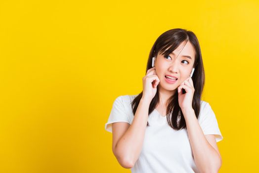 Portrait Asian of a happy beautiful young woman wear wireless earphone listening to music from smartphone having fun and dancing to sounds of favorite music studio shot isolated on yellow background