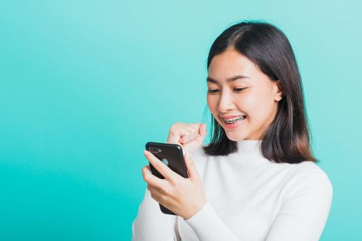 Asian woman smile holding smartphone she happy and surprised after received message, female excited cheerful her reading mobile phone some social media isolated on blue background, Technology concept