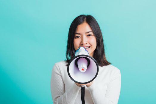 Beautiful Asian woman smile she holding megaphone making the announcement, female excited cheerful announce good news isolated on a blue background