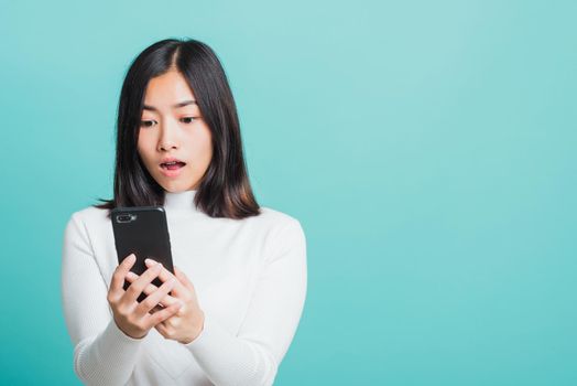 Portrait female anxious scared on the phone seeing bad news, Young beautiful Asian woman surprised shocked with mobile phone close mouth with palm, studio shot isolated on a blue background