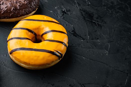 Donut with orange glaze and colorful sprinkle, on black background with copy space for text
