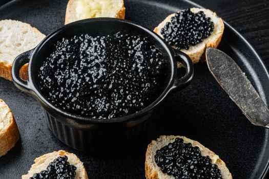Black caviar served on baguettes, on black wooden table background