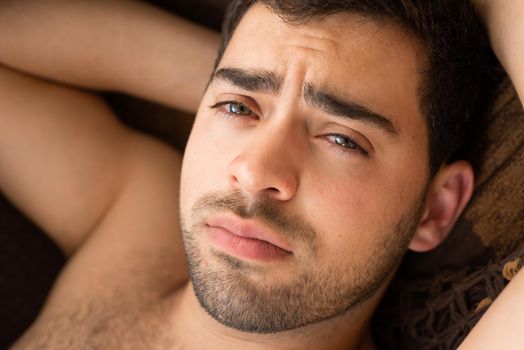 Closeup portrait of unshaven young guy in a hammock, looking at camera.