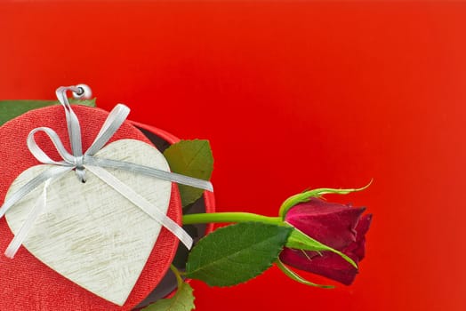 Single rose on gift box and heart medallion over red background with free copy space