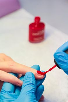 close-up of a woman applying red nail polish. Women's beauty service