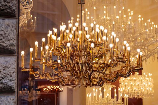 Expensive luxury large chandelier behind glass with gilding. Reflection in the shop window. Lights in the form of candles.