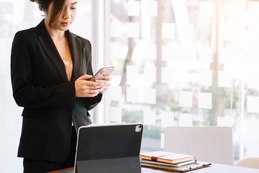 Businesswoman working on smart tablet at office while using smartphone for social or chat.