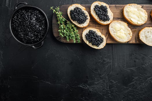 Black caviar served on baguettes, on black background, top view flat lay with copy space for text