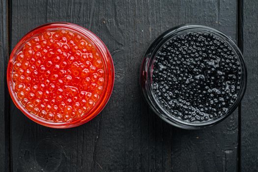 Glass jar with black and red caviar, on black wooden table background, top view flat lay