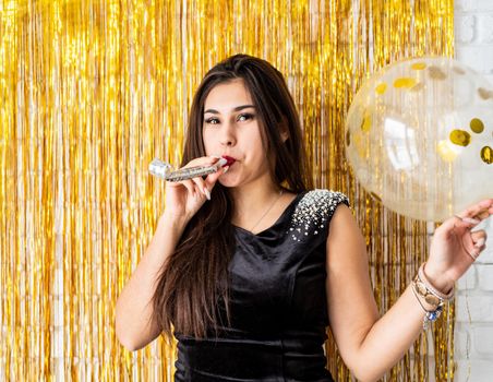 Birthday party. Beautiful brunette woman in black party dress celebrating her birthday blowing the noise maker