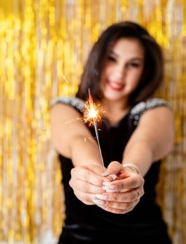 Birthday party. Beautiful young woman holding sparkler and balloon on golden background