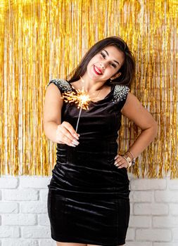 Birthday party. Beautiful young woman holding sparkler and balloon on golden background