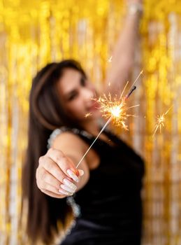 Birthday party. Beautiful young woman holding sparkler and balloon on golden background