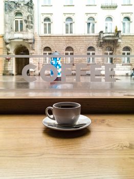 Small white coffee cup in cafe in front of window with coffee word sticker