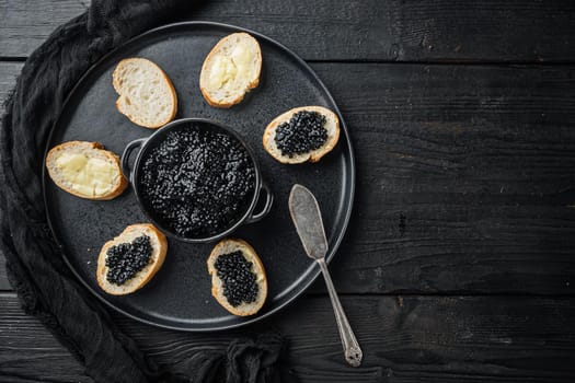 Black caviar served on baguettes, on black wooden table background, top view flat lay with copy space for text