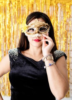 Birthday party. Beautiful brunette woman in black party dress wearing shiny golden masquerade mask