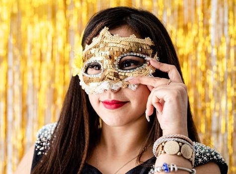 Birthday party. Beautiful brunette woman in black party dress wearing shiny golden masquerade mask
