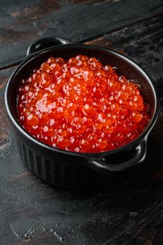 Red caviar black bowl, on old dark wooden table background