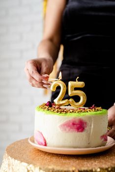 Birthday party. Caucasian woman in black party dress lighting candles on birthday cake