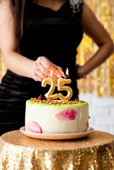 Birthday party. Caucasian woman in black party dress lighting candles on birthday cake