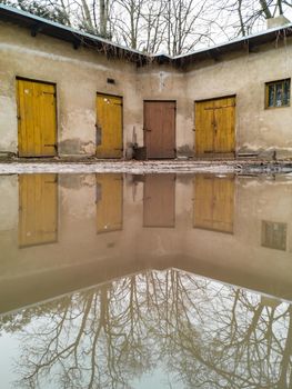 Small building with few doors reflected in small puddle