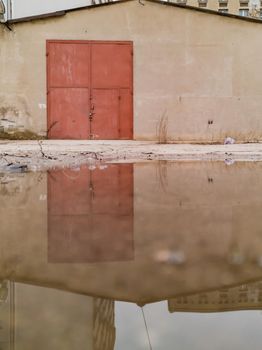 Facade of big garage with red gate reflected in puddle