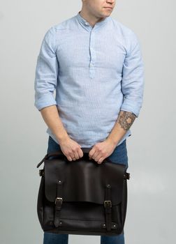 Brown men's shoulder leather bag for a documents and laptop holds by man in a blue shirt and jeans with a white background. Satchel, mens leather handmade briefcase