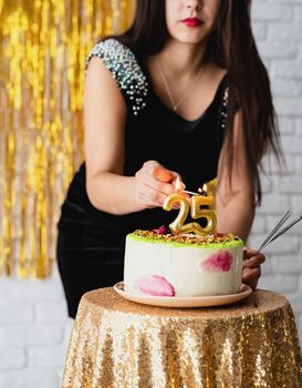 Birthday party. Beautiful brunette woman in black party dress celebrating her birthday light the candles 25 on the cake