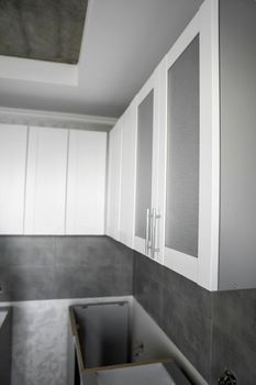 Custom kitchen cabinets installation with a white furniture facades mdf. Gray modular kitchen from chipboard material on a various stages of installation. A frame furniture fronts mdf profile