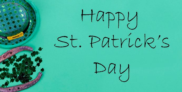 St Patricks day holiday celebration with Irish elf hat, horse shoe and small clovers on a green paper background with copy space plus added text message