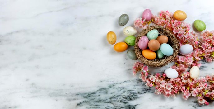 Happy Easter holiday concept with nest of colorful eggs with pink cherry blossom flowers on stone background in overhead view 