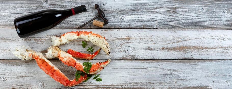 King crab claws and legs with wine bottle on white rustic wood in flat lay format 