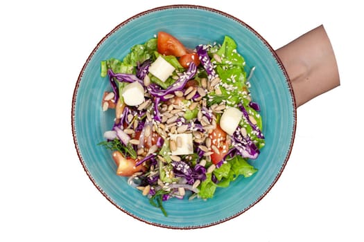 A plate of fresh, delicious salad on a white background, isolate. Salad with lettuce, tomatoes, seeds, cucumbers and cheese. The view from the top.