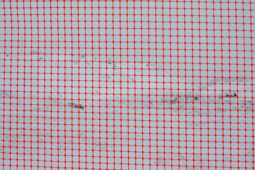 Plastic red safety net for construction site. Fencing repair work on the street. Construction grid on the background of winter snow