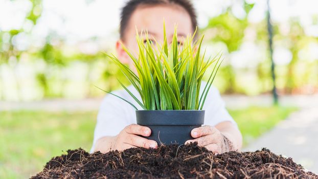 World Environment Day Environment and Save World Concept, Hand of Asian cute cheerful little child boy planting young tree on black soil on green garden background