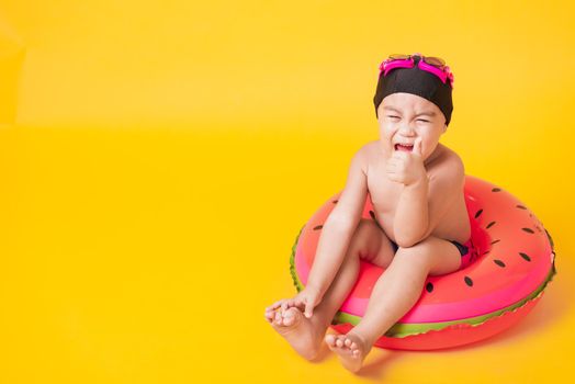 Summer vacation concept, Portrait Asian happy cute little child boy wear goggles, swimsuit hold beach watermelon inflatable ring, Kid have fun sit in inflatable, studio shot isolated yellow background