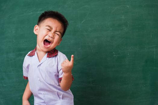 Back to School. Happy Asian funny cute little child boy from kindergarten in student uniform smiling point finger to side away space on green school blackboard, First time to school education concept
