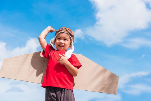 Happy Asian funny child or kid little boy smile wear pilot hat and goggles play toy cardboard airplane wing flying raises hand up against summer blue sky cloud background, Startup freedom concept