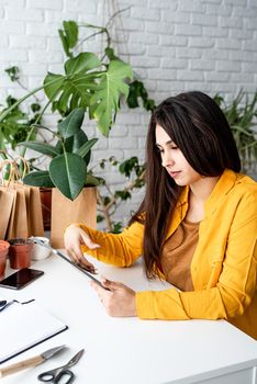 Home gardening. Small business. Woman gardener working on digital tablet surrounded with plants