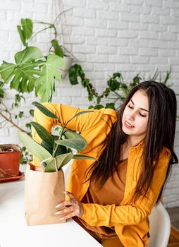 Home gardening. Small business. Young woman gardener taking care of the plants putting a flowerpot to the craft bag ready to sell it